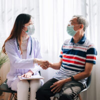 Asian doctor visit and examines a senior man at home ,shaking hands after finished health check up ,hospital services ,and wearing a mask to protect covid-19.